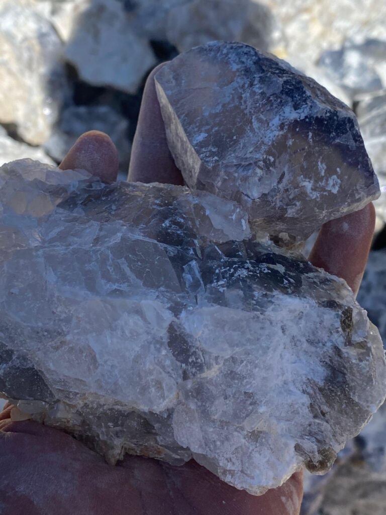 Hand holding raw fluorite (fluorspar) crystals with translucent white and grey tones, used in metallurgical and chemical industries.